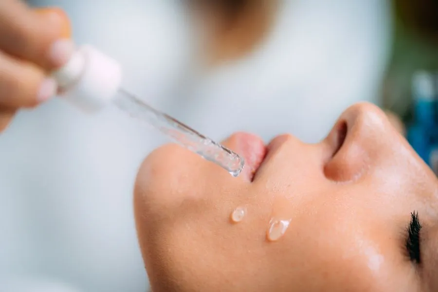 A close up of a women dropping serum onto her cheek.